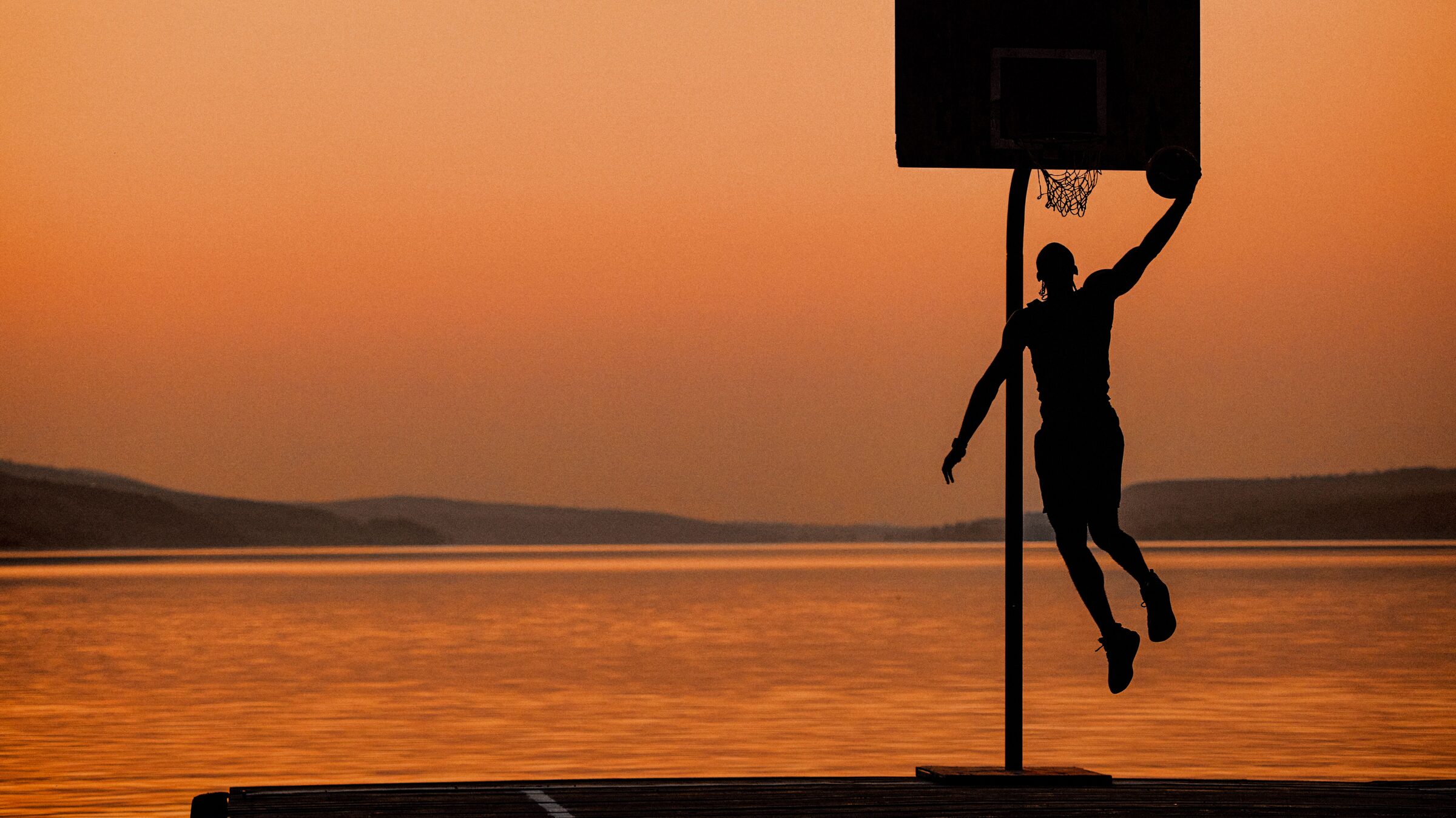 A player dunks at sunset on a lakeside court