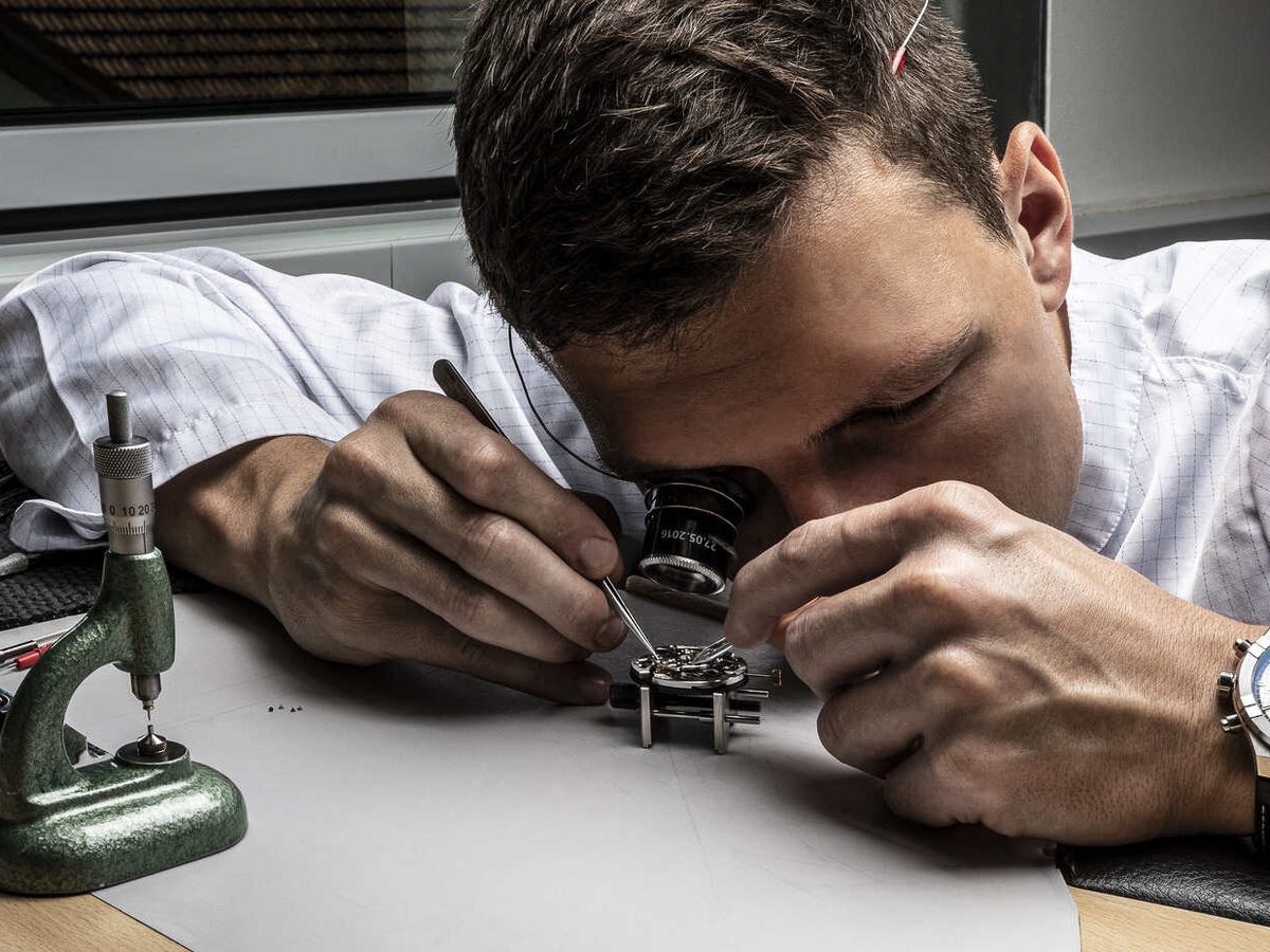 A watchmaker examines a Maurice Lacroix movement through a loupe at the bench